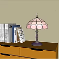 Stained Glass Table Lamp With Pink Blue Shade Black Base On Wooden Shelf With Books
