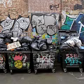 Public Trash Bins Against Graffiti Covered Brick Walls With Overflowing Trash And Art