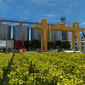 Industrial Plant With Silos Yellow Gantry Crane Truck And Yellow Flowers Field Under Blue Sky