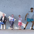 Group of People Sitting Standing Against Gray Wall on Light Floor With Child Pom Poms