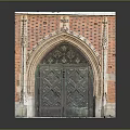 Ornate Red Brick Archway Featuring Carved Details And Wooden Double Doors With Intricate Patterns