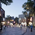 Vibrant Commercial Street with Pedestrians Trees Cafes Buildings and Evening Lighting