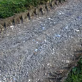 Rutted Gravel Ground With Grass Edges Visible Tire Tracks And Loose Stones