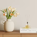 White Ceramic Vase With Cream And Orange Tulips Next To Reed Diffuser And Stacked Books