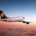 Lufthansa Passenger Airliner Flying Over Clouds And Mountain Ranges In Sunset Sky
