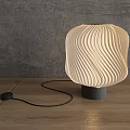 Modern Wavy Lampshade Table Lamp With Warm Light On Wooden Table Against Gray Wall