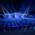 Formal Event Venue With Blue Lighting Rows Of Chairs And Stage Screens