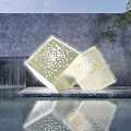 Golden Perforated Cube Sculptures on Waterfront Platform with Waterfall Reflection and Green Plants