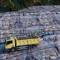 Scenic Landscape Featuring Yellow Dump Truck On Rocky Textured Ground With Puddles And Trees