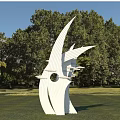 White Streamlined Sculpture With Curved Lines On Green Lawn Among Trees Under Blue Sky