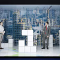 Two men discussing large white block models against industrial city backdrop