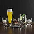 Assorted Drinking Glasses With Foamy Yellow Drink Ice Lime And Candle On Dark Wood Table