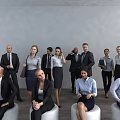 Group of Business Professionals Standing and Sitting in Office With Gray Wall and Wooden Floor
