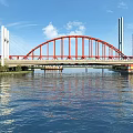 Red Arch Bridge With White Towers Spanning Calm Water Under Blue Sky And Clouds