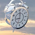 Silver Alarm Clock With White Dial And Black Numbers Against Sky Clouds Background