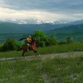 Scenic Green Hills Grassland with Snow Capped Mountains under Cloudy Sky and Rider on Horseback