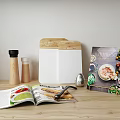 Essential Kitchen Utensils on Wooden Tabletop with Open Magazine Pepper Grinders Cutting Board and Cookbook