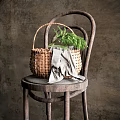 Woven Vase With Green Flowers Resting On Wooden Chair With Gray Cloth And Dark Background