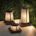 Outdoor Lamps With Fabric Shades And Black Metal Frames On Stone Patio With Greenery Background