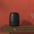 Black Wireless Speaker on Wooden Table with Orange Wall and Black Vase with Pink Flowers