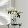 Transparent Glass Vase With White Flowers On Round Metal Table By Window Blinds