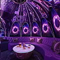 Modern KTV Lounge With Purple Lighting Arched Structures Neon Rings Sofas Table Drinks And Fruits
