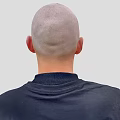 A Bald Head Man in Black Turtleneck Sweater with Silver Necklace Against Light Gray Background