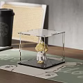 Cute Yellow Doll In Clear Transparent Display Case Placed On Table With Green Mat Background