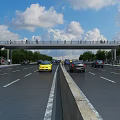 Pedestrian Bridge Over Wide Highway With Pedestrians Vehicles Trees Blue Sky And White Clouds