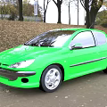 Green Hatchback Car Parked On Roadside With Trees Autumn Leaves And Park Background