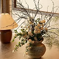 Natural Ceramic Vase With White Flowers Green Foliage And Slender Branches On Tabletop Indoor Setting