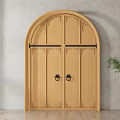 Wooden Double Doors with Arched Top and Carved Details Near Green Plant on Gray Wall