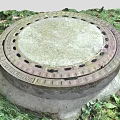 Circular Manhole Cover With Metal Frame In Outdoor Grass And Fallen Leaves Scene