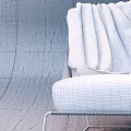 Modern Leisure Chair with Woven Fabric Black Metal Frame and Brown Blanket Against Concrete Wall