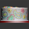 White Round Cake With Colorful Rainbow Flower Paisley Designs And Red Border On Reflective Plate