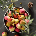 Ceramic Bowl Filled With Fresh Apples And Olive Branches On Dark Countertop With Pine Cone Nearby