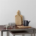 Carved Wooden Cutting Board With Black Kettle And Glass Bowls In Kitchen Setup