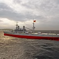 Large Battleship With Red And White Hull Sailing On Open Sea Under Cloudy Sky