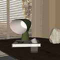Green Table Lamp Illuminates On Books With Small Cup And Stone Near Window Blinds