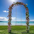 Scenic Seaside Flower Arch With Swing On Green Grass Under Blue Sky