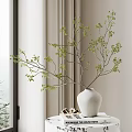 White Ceramic Vase with Green Branches and Small Leaves Placed on Magazines by Window Curtain