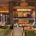 JOHOBUS Bar Interior With Green Plants Tables And Liquor Displays