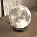 Illuminated Moon Shaped Lamp on Wooden Table with Black Base and Geometric Art Print