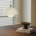 Modern White Pendant Light Hanging Above Wooden Table With Bowl And Books Near Window Blinds