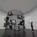 Art Installation Featuring Wire Mesh Cylinder Multiple TV Screens Black And White Images Person Pointing