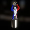 White Statue With Blue Red Arms Holding Circular Object Above Head On Silver Cylindrical Base