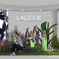 LALIQUE Exhibition Showcase With Colorful Flowers Green Plants And Person Pointing