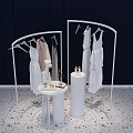 White Display Racks Hanging White Dresses With Round Table Cylindrical Stand Dark Background Pebble Floor