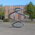 Outdoor Spiral Staircase In Plaza Area With Spiral Design Red Brick Building And Green Trees