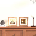 Two Wooden Frames with Floral Art and Interior Scene on Wooden Cabinet with Table Lamp